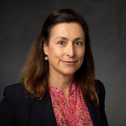 Headshot of Simone Dzuba, a middle age woman smiling on a simple light black background.