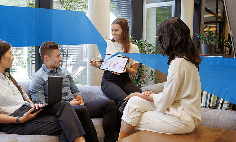 Three female and one male student are sitting in a lounge. One student holds a tablet and shows something on it.