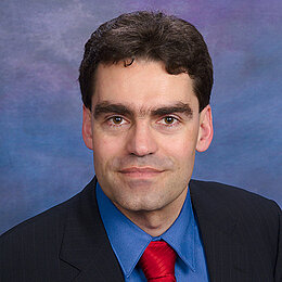 Headshot of Prof Dr Tim Buethe, a middle age man smiling on a simple blue background.