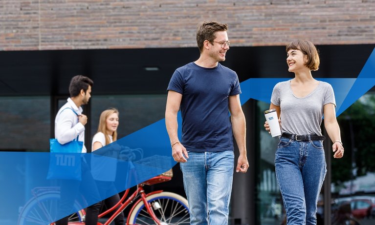Two students, one male, one female walking across campus Heilbronn together. Two students with a bike in the background.